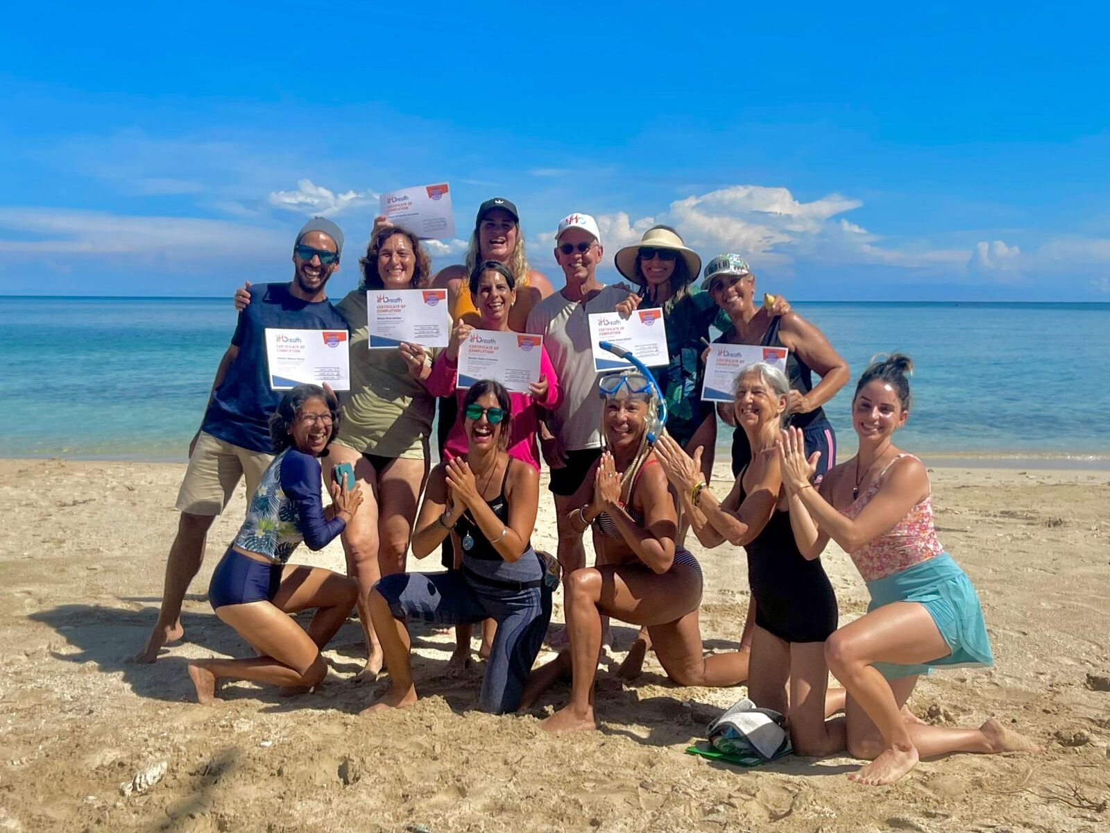 Graduates on a beach holding their certificates