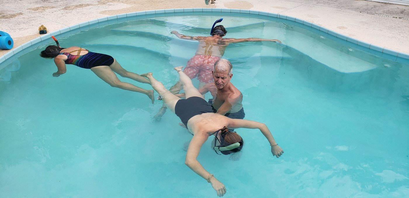 Roberto standing in a pool beside a woman floating face down with a snorkel during a water breathing session