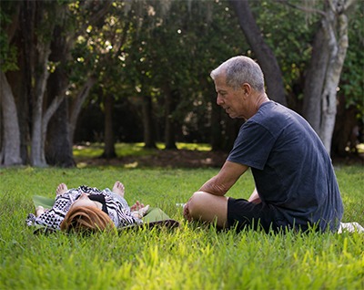 Roberto sitting on the grass beside a client lying down during an outdoor session