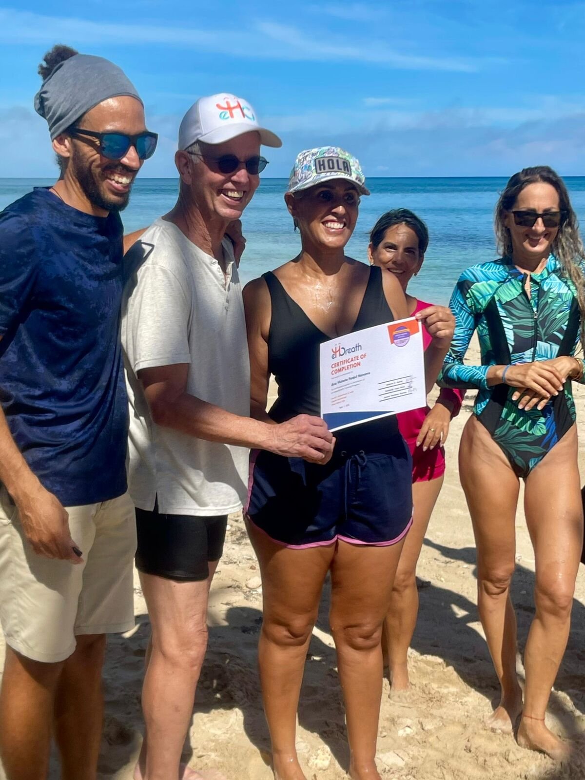 A graduating group on a beach, certificates in hand