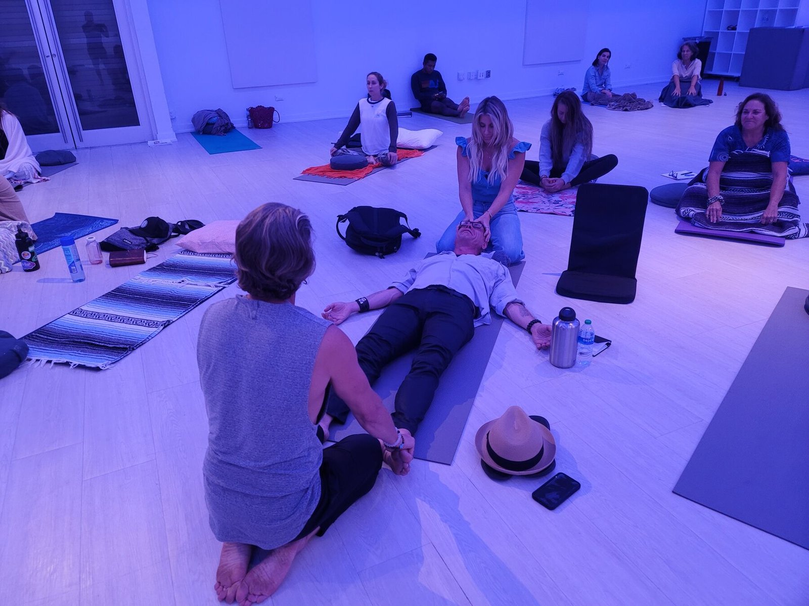 A trainee guides a client lying on a mat while other students practice around the room