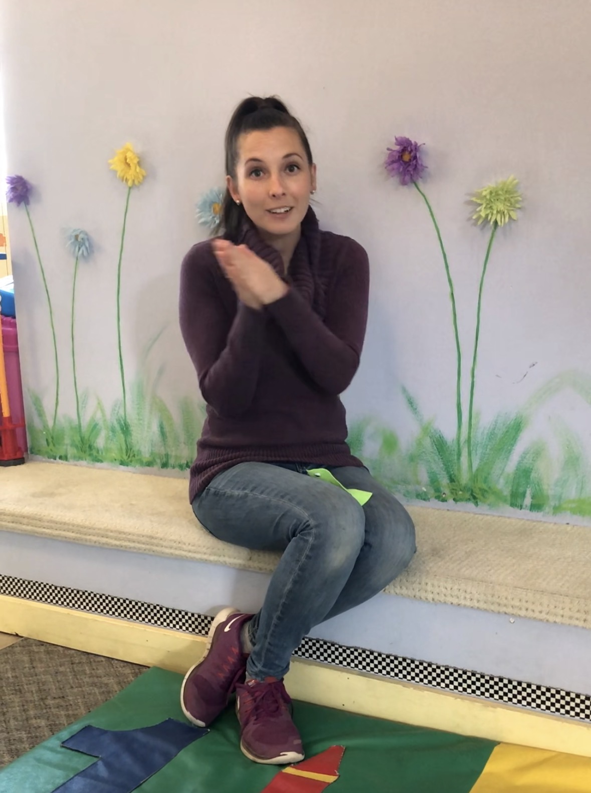 Kierstin in her daycare classroom in front of a painted flower wall