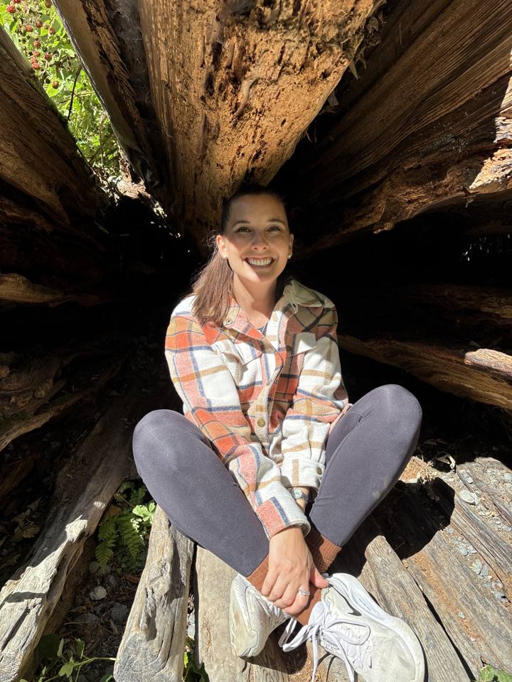 Kierstin smiling in the forest, sitting inside a big old tree