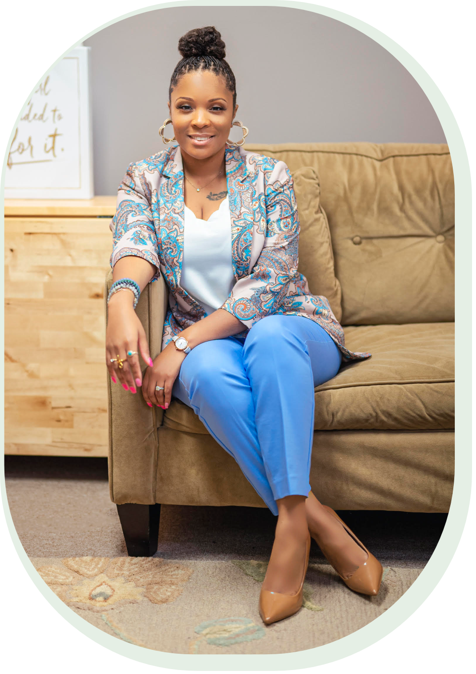 Christina Simmons seated on a tan couch, wearing a patterned jacket and blue pants