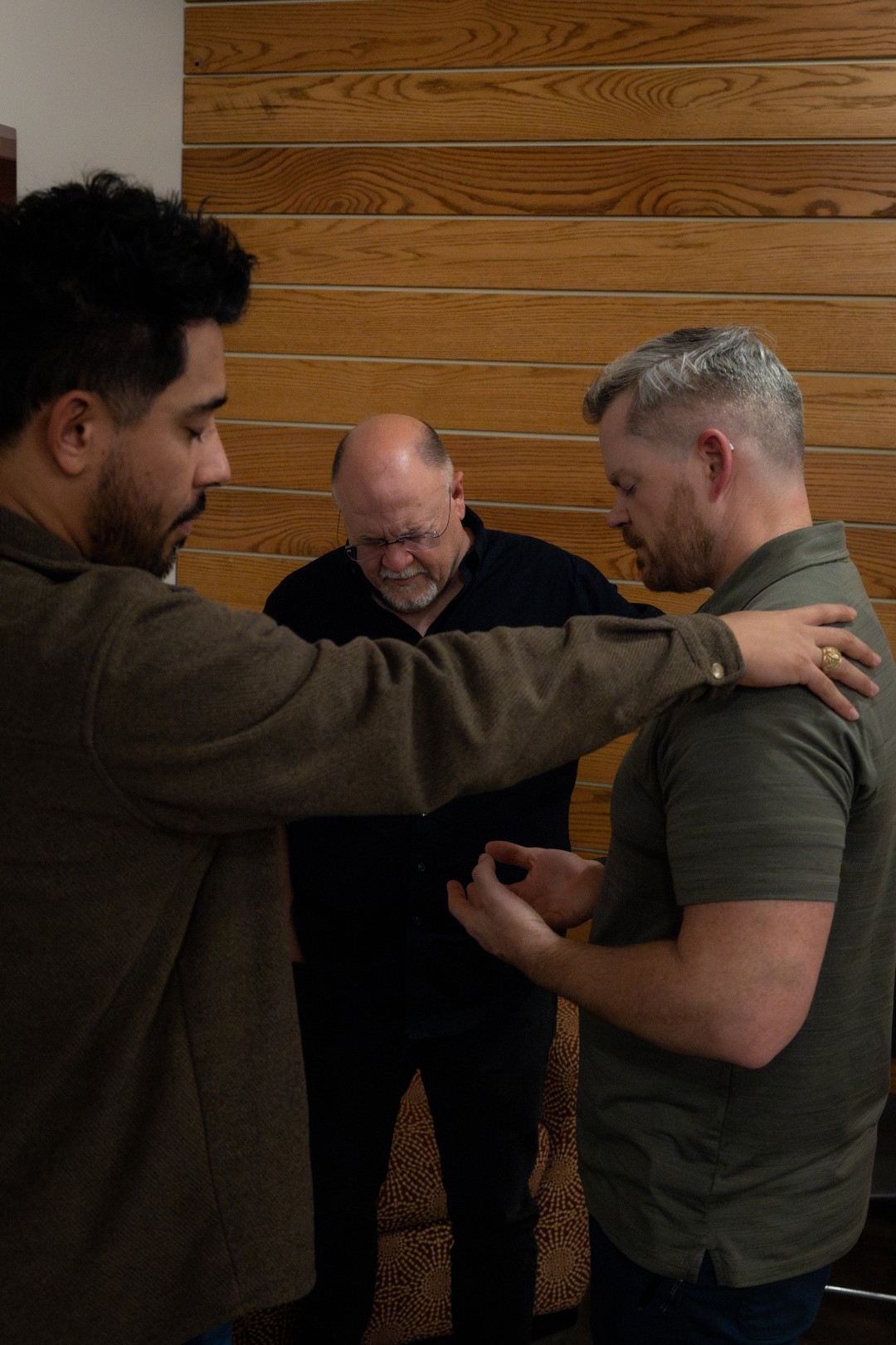 Roundtable participants praying with a hand on one another's shoulder