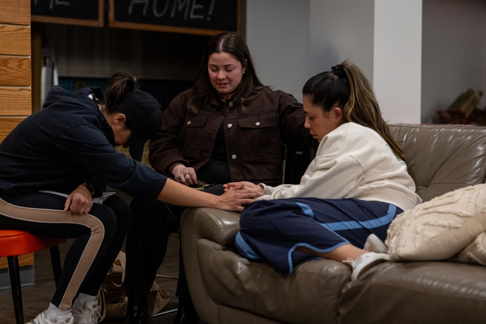 Three women holding hands in prayer during a Roundtable small-group time