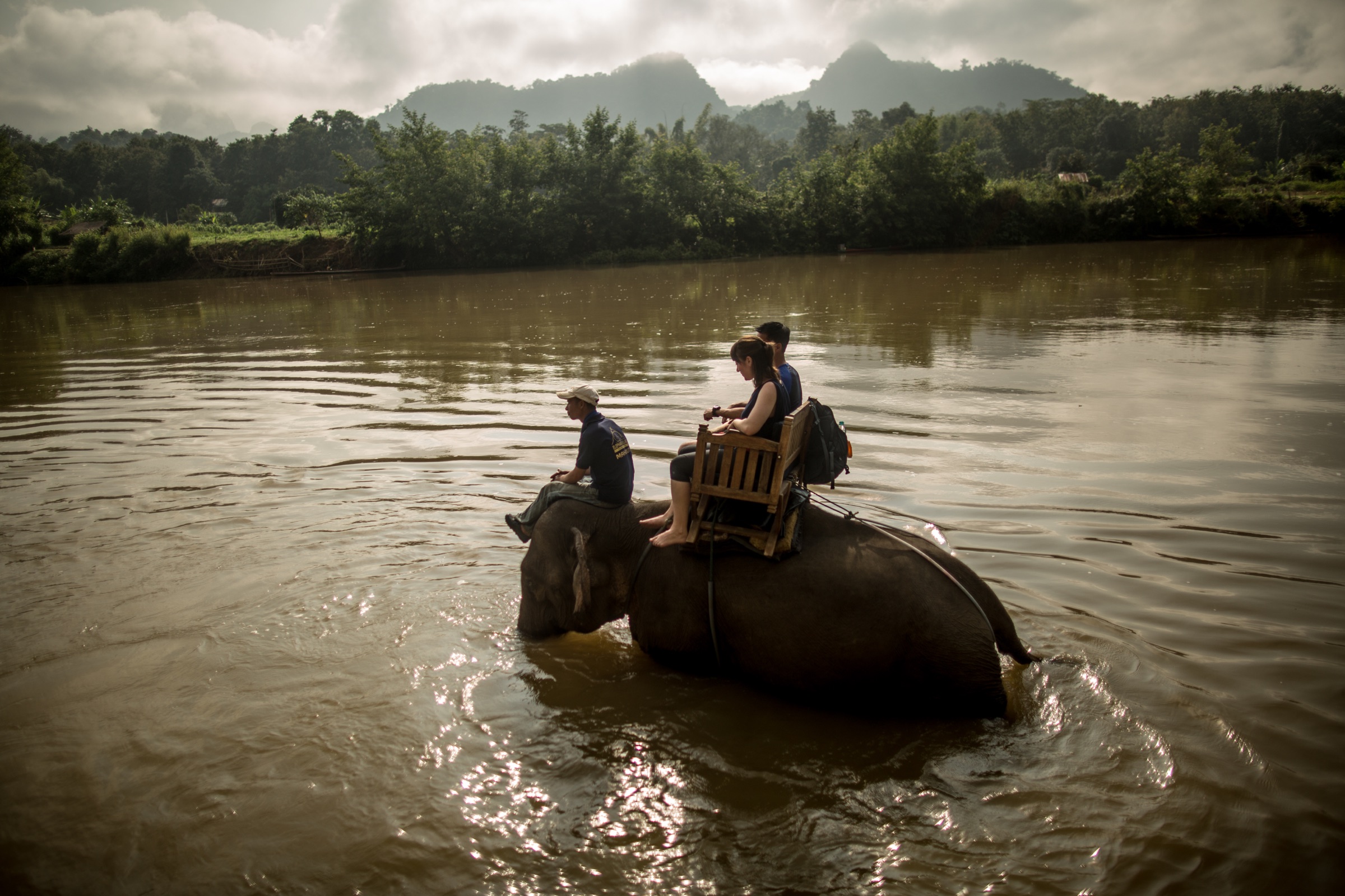 Tourists seated on an elephant as it wades through a river in Luang Prabang, Laos.