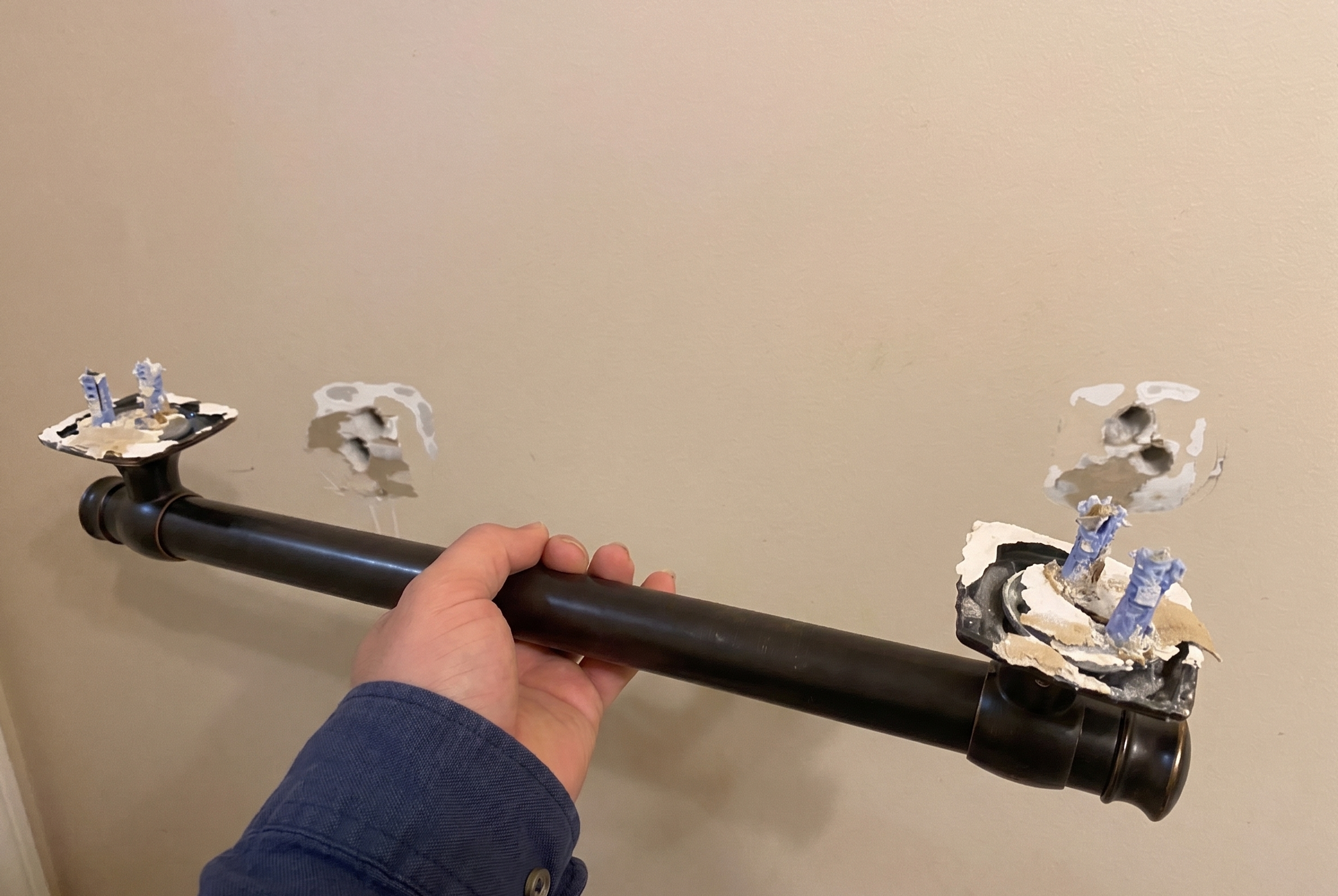 A grab bar pulled out of the wall, with chunks of drywall and blue anchors still clinging to the flanges.