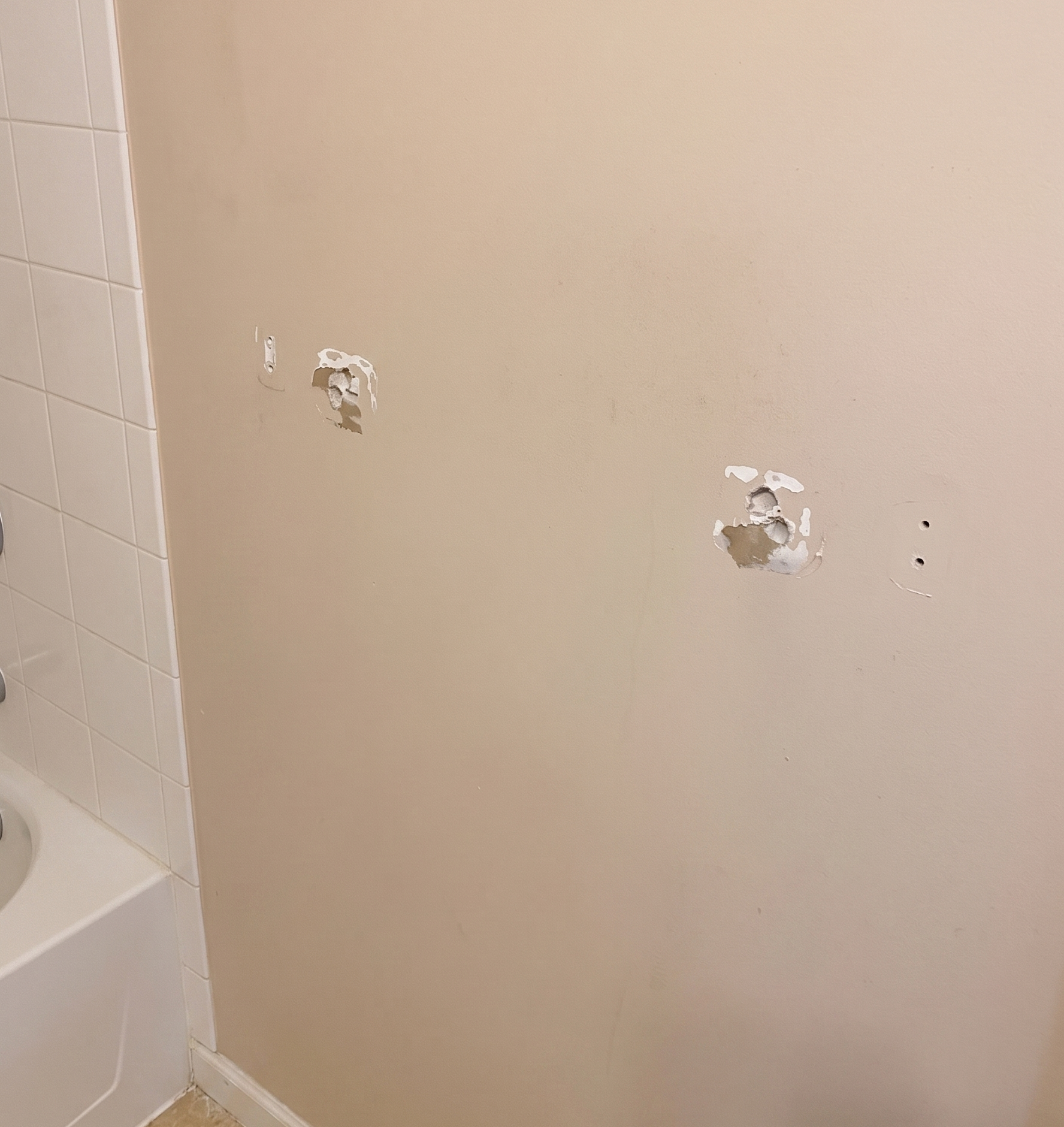 Blown-out drywall where a grab bar was pulled out of the wall, with anchor fragments still embedded.