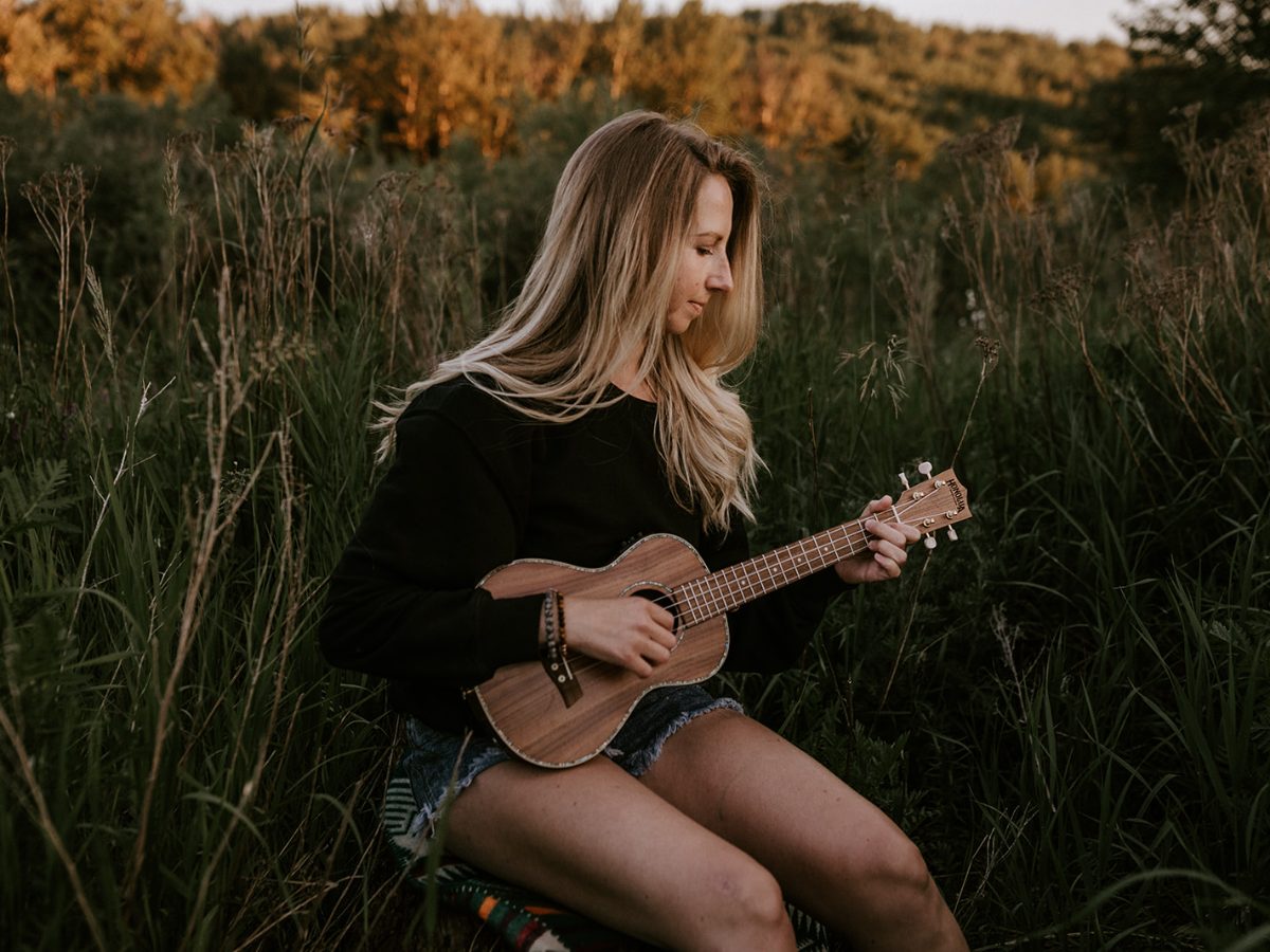 A learner playing a song on her ukulele outdoors at golden hour