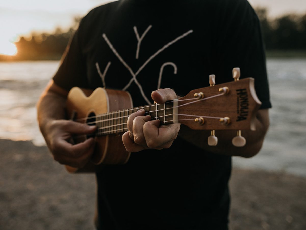 Close-up of fingers forming a chord on a ukulele fretboard in warm evening light