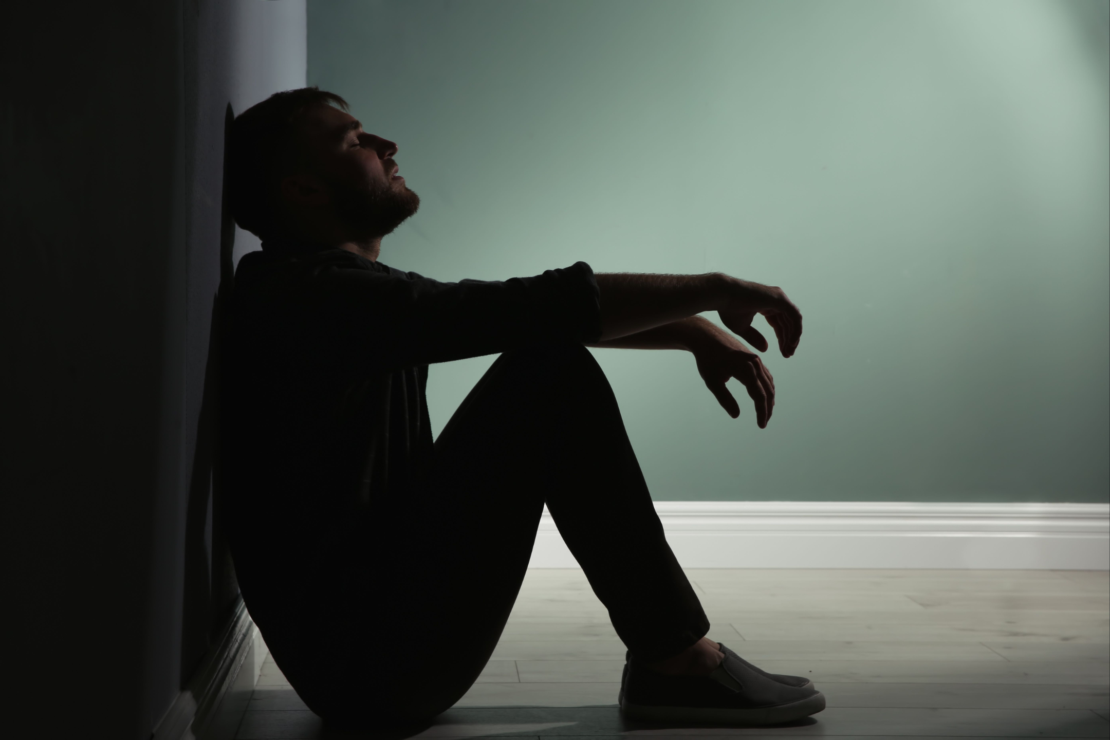 Man sitting on the floor in a dim room, looking exhausted and overwhelmed