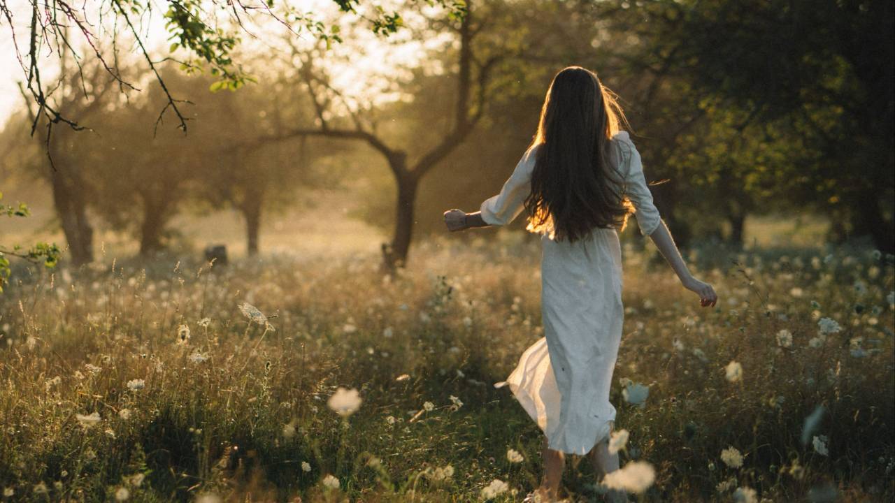 A woman walking barefoot through a sunlit meadow, symbolizing childhood freedom, body awareness, and reconnecting with yourself through Myofascial Release and Presence Centered Awareness Therapy at Sol Bodyworks.