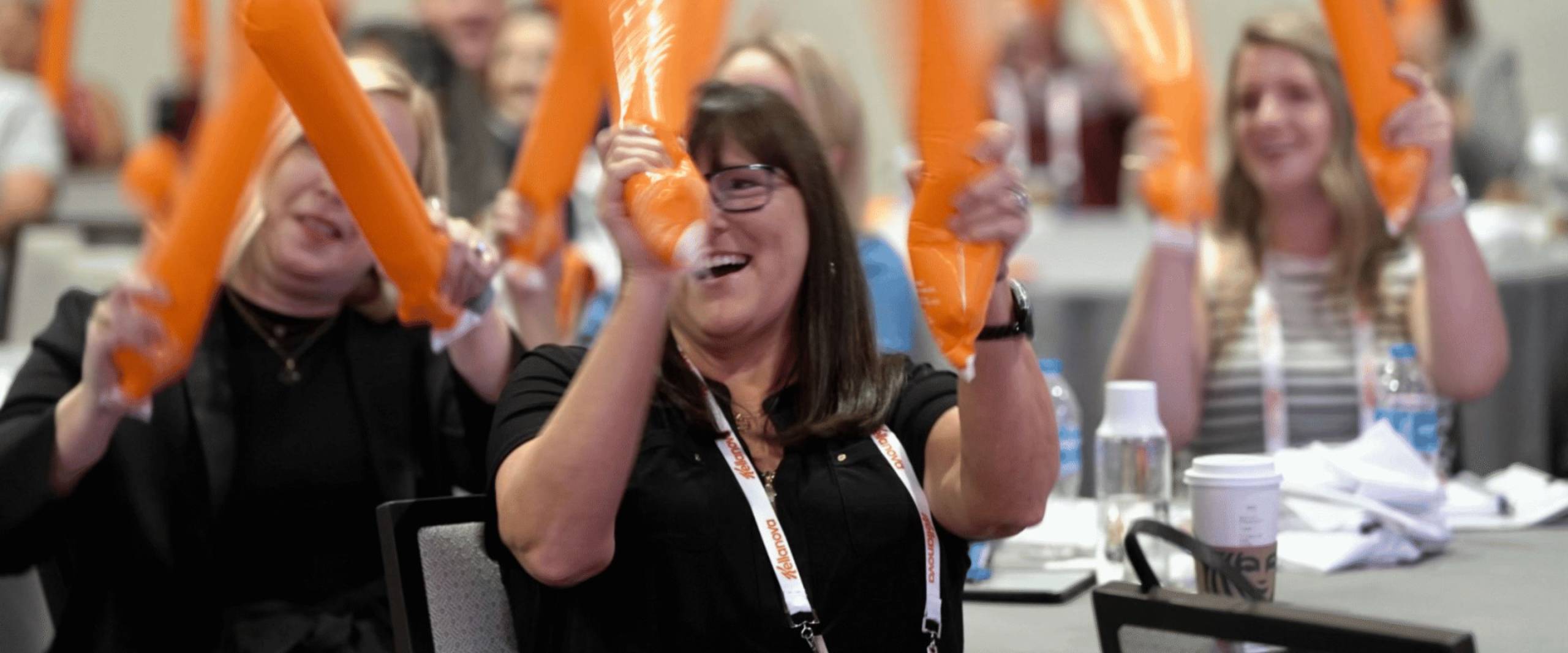 Smiling conference attendees participate in an interactive corporate drumming activity led by healthcare keynote speaker Mike Veny using orange percussion tubes.