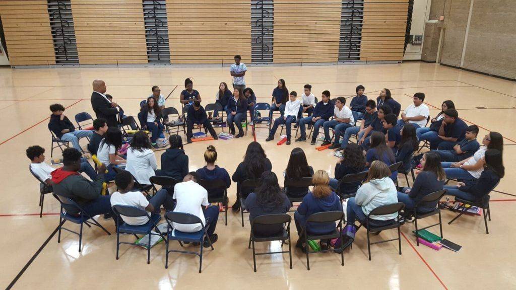 Mike Veny leads K-12 students in an interactive drumming team-building activity in a school gymnasium.