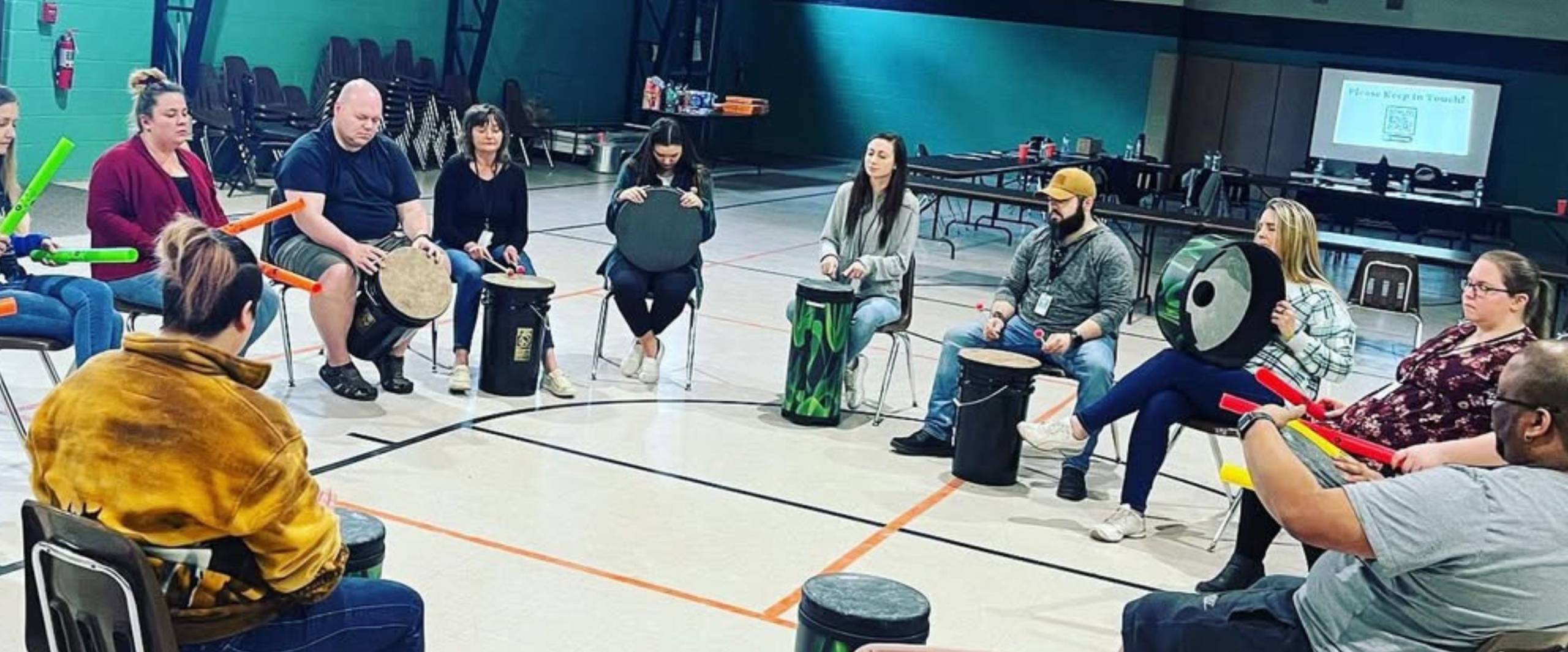 Employees participate in a corporate drumming team-building workshop with Mike Veny using drums and percussion tubes.