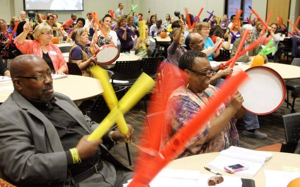 Conference attendees play percussion instruments during an interactive corporate drumming team-building icebreaker with Mike Veny.