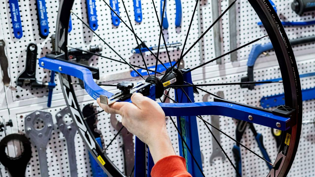 A mechanic adjusting a bicycle wheel at a real workshop bench.