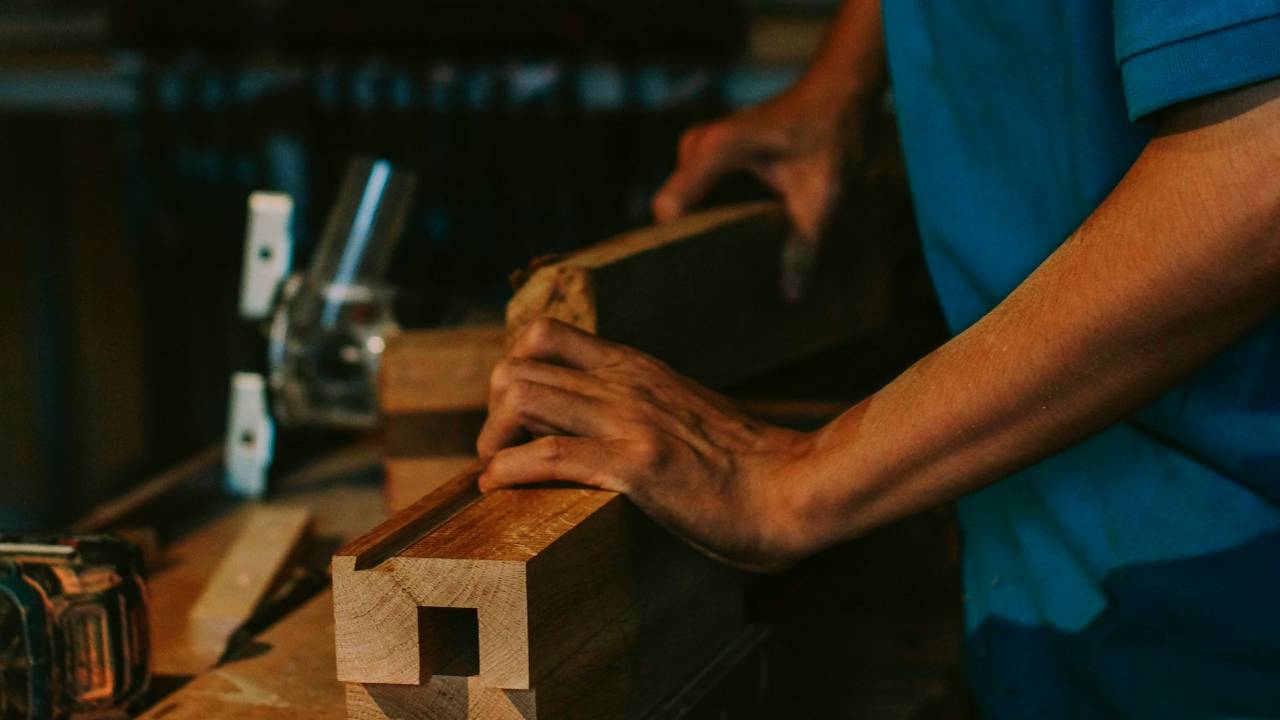 A carpenter shaping wood by hand at a working shop bench.