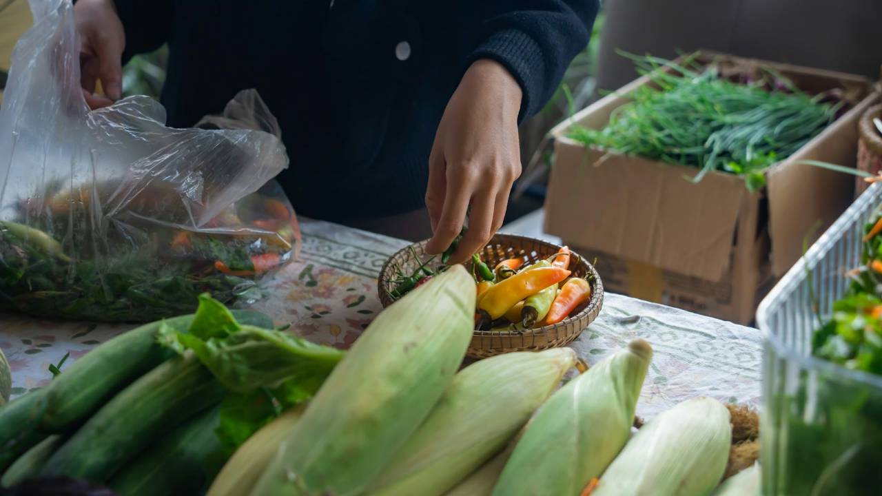 A shopper selecting fresh vegetables at a real market stall.