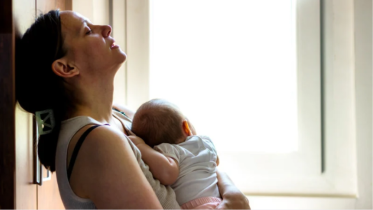 Caregiver leaning against a wall with eyes closed while holding a baby