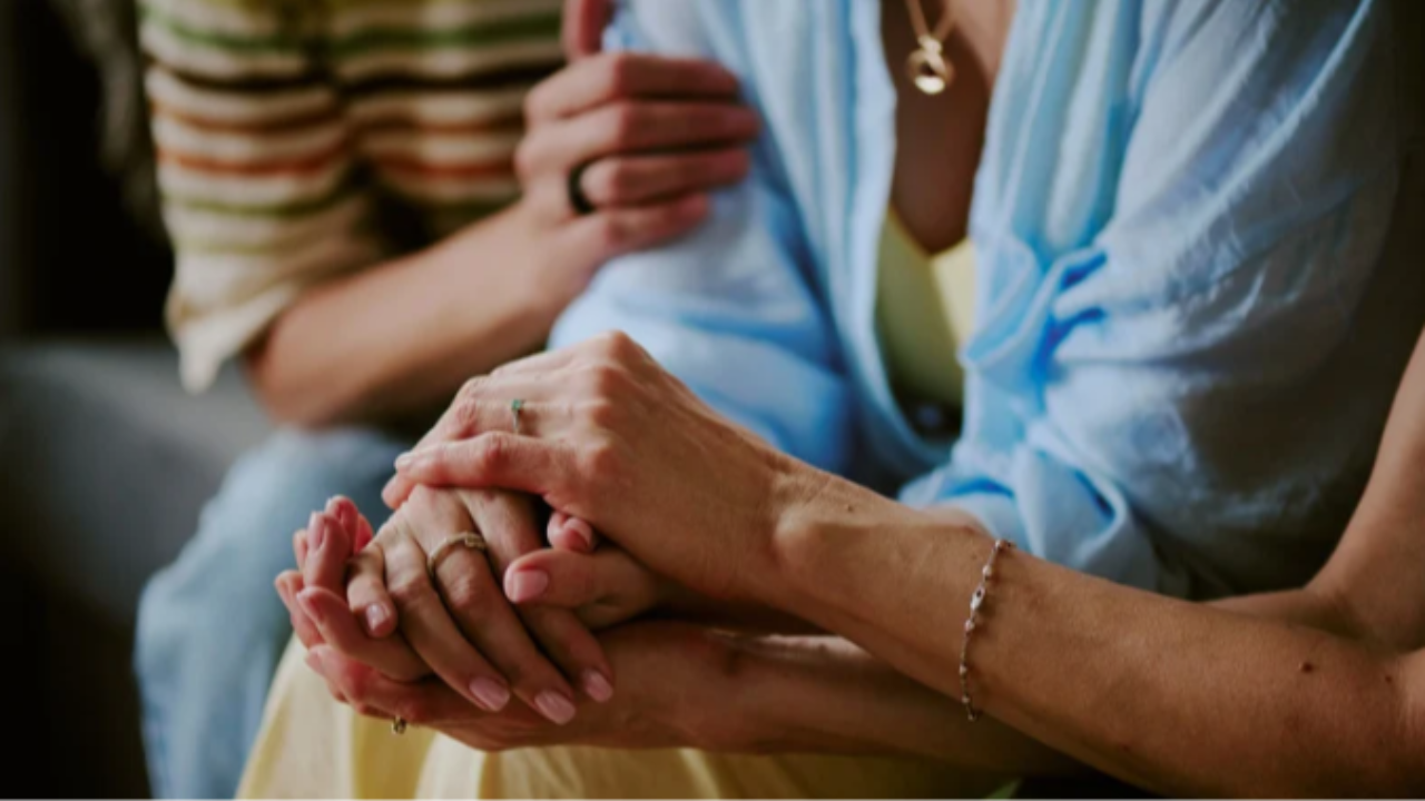 Three people sitting together, one holding another’s hands in a caring gesture