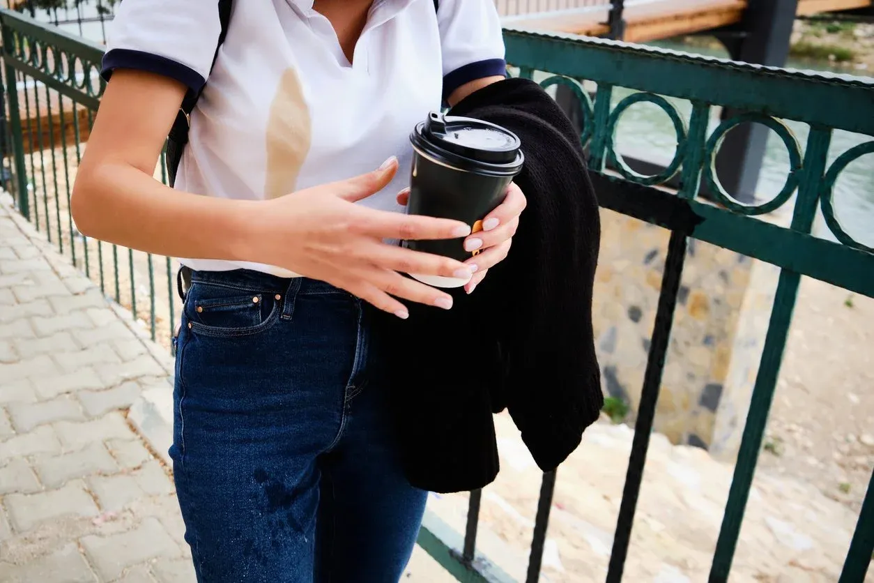 Frazzled young woman with coffee spill on her shirt, carrying coffee and looking overwhelmed