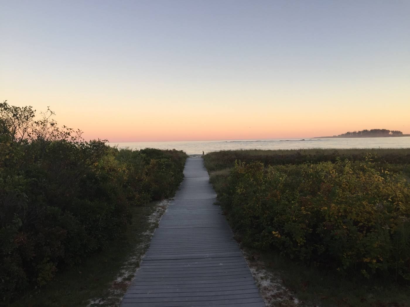 A boardwalk path toward the sea at dusk
