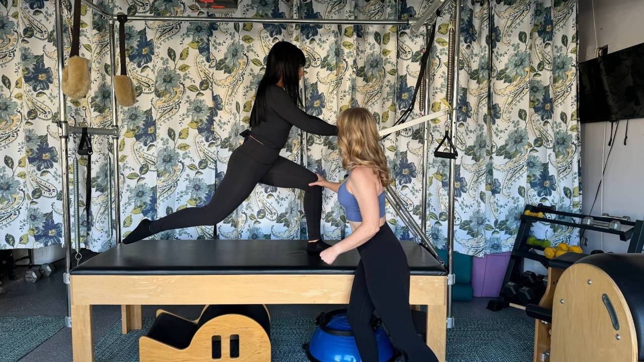 Pilates instructor guiding a woman through an exercise on a Cadillac