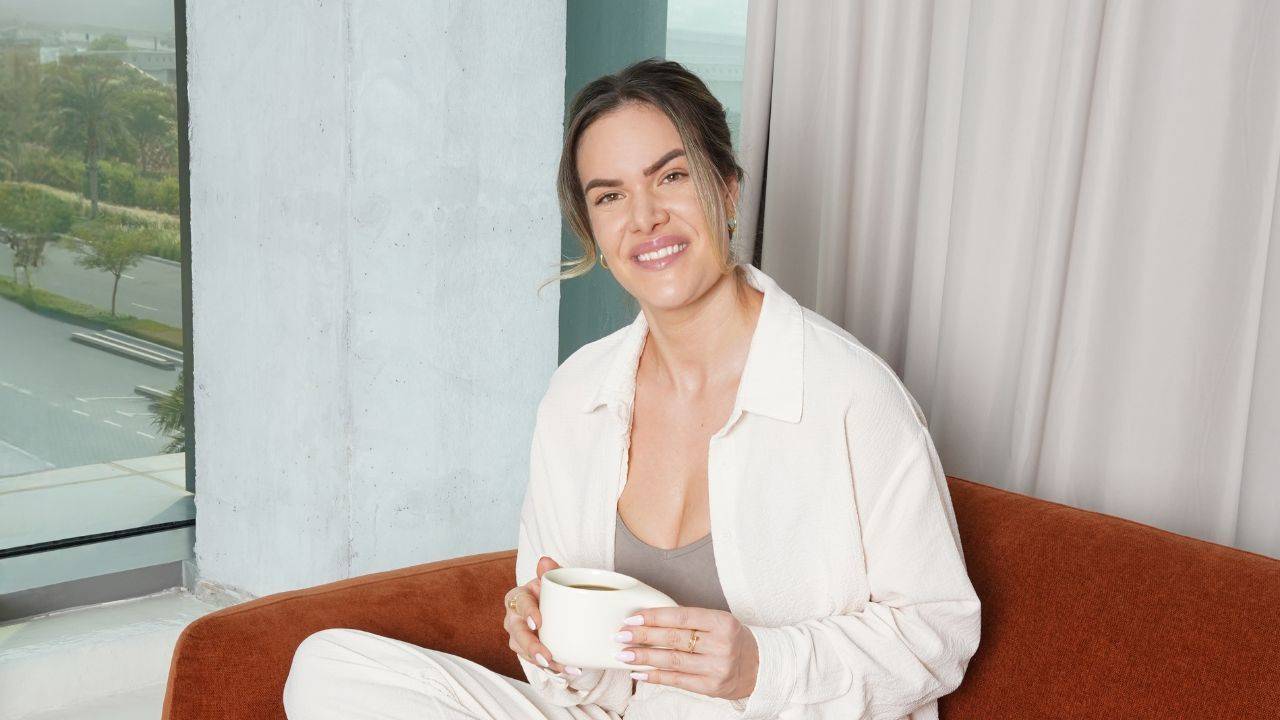 Amanda Louise sidder i en sofa med en kop kaffe i hænderne i dagslys.