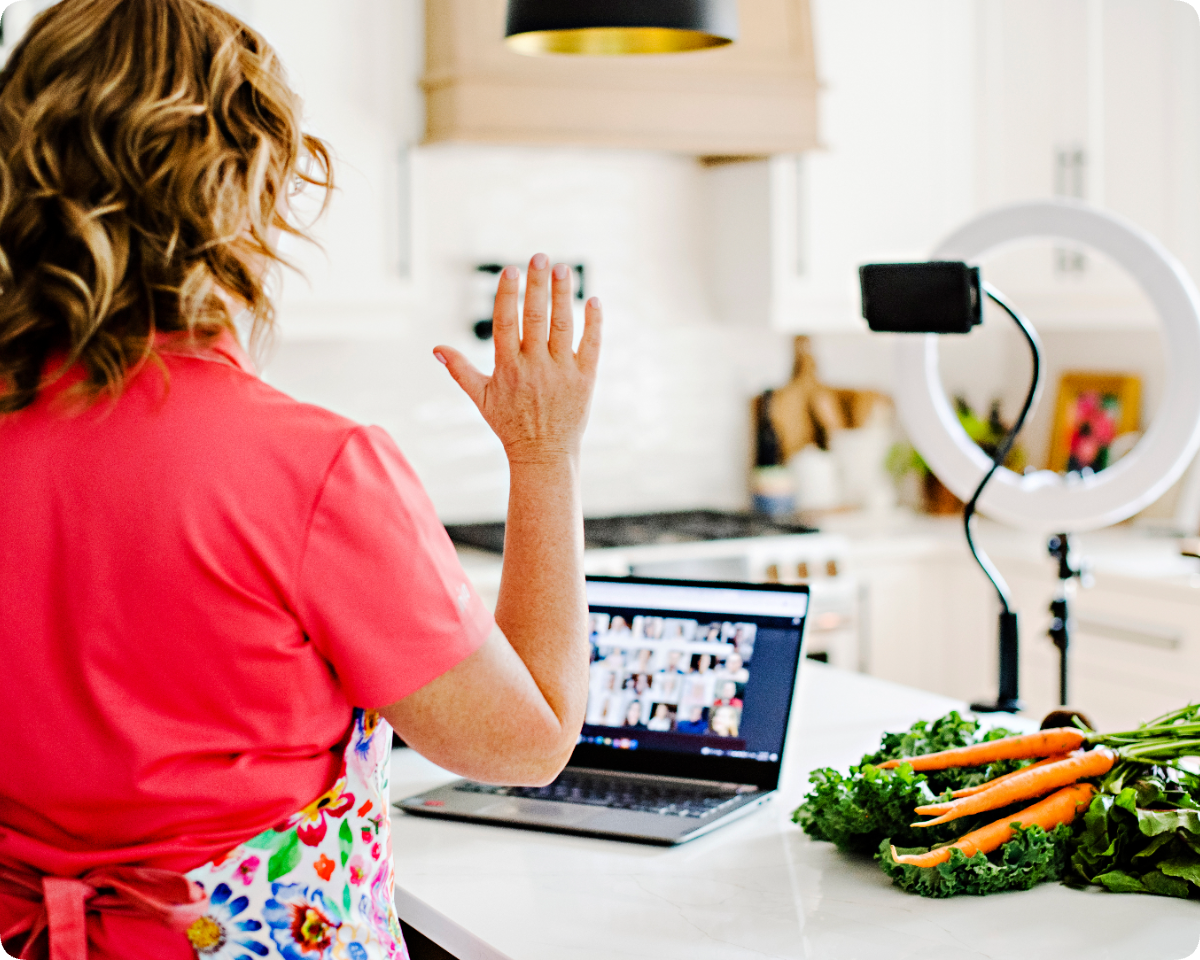 Woman filming an online cooking class in her kitchen with a ring light and laptop