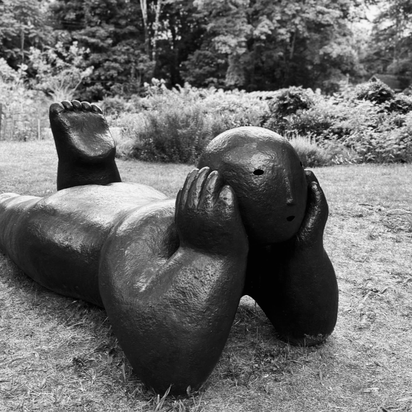 Bronze statue of person lying on their belly in the grass contemplating life
