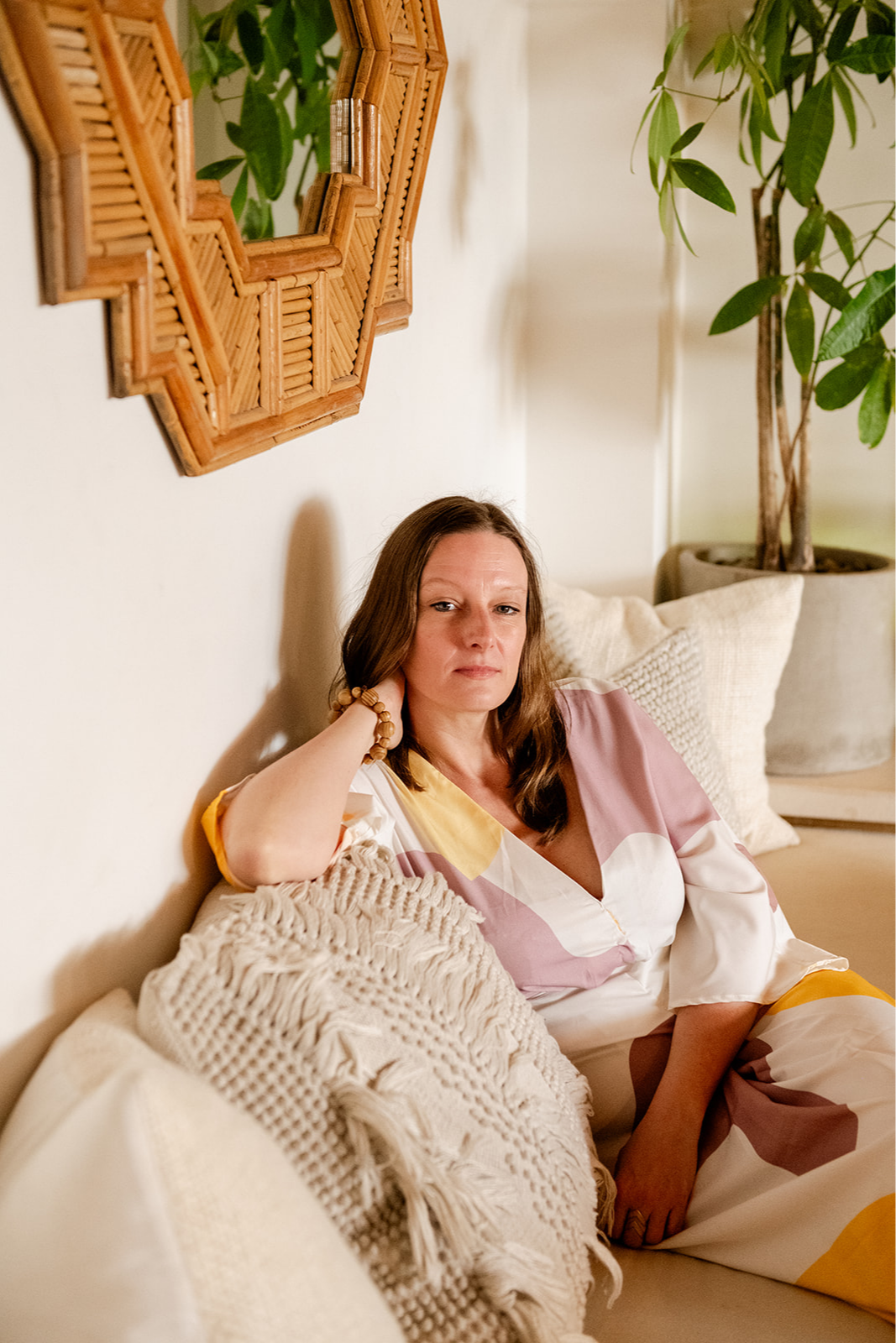 Pamela relaxing on a sofa beneath a rattan mirror