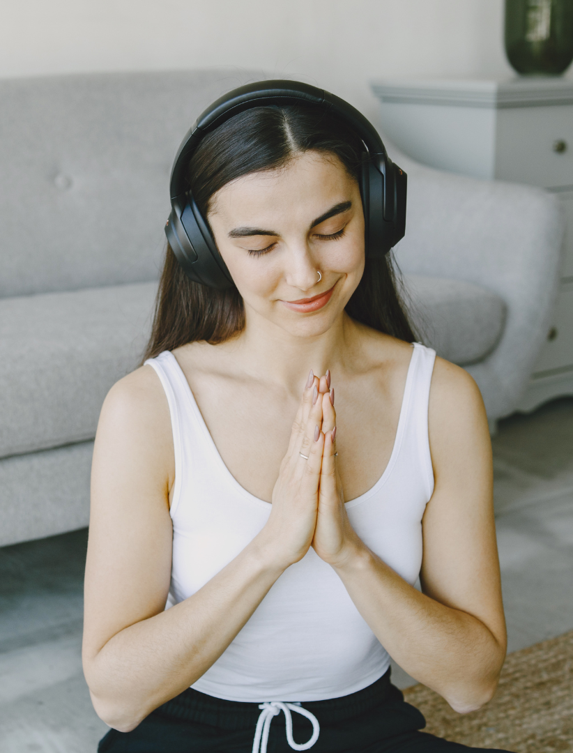 woman with dark hair sitting in meditation with headphones on and hands at heart