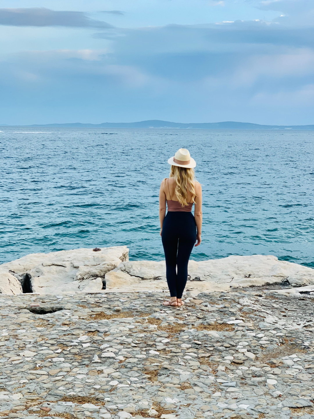 A photo of Rebecca Michelle a personal mindfulness coach from nyc. She is looking at the sea and has a beige hat on.