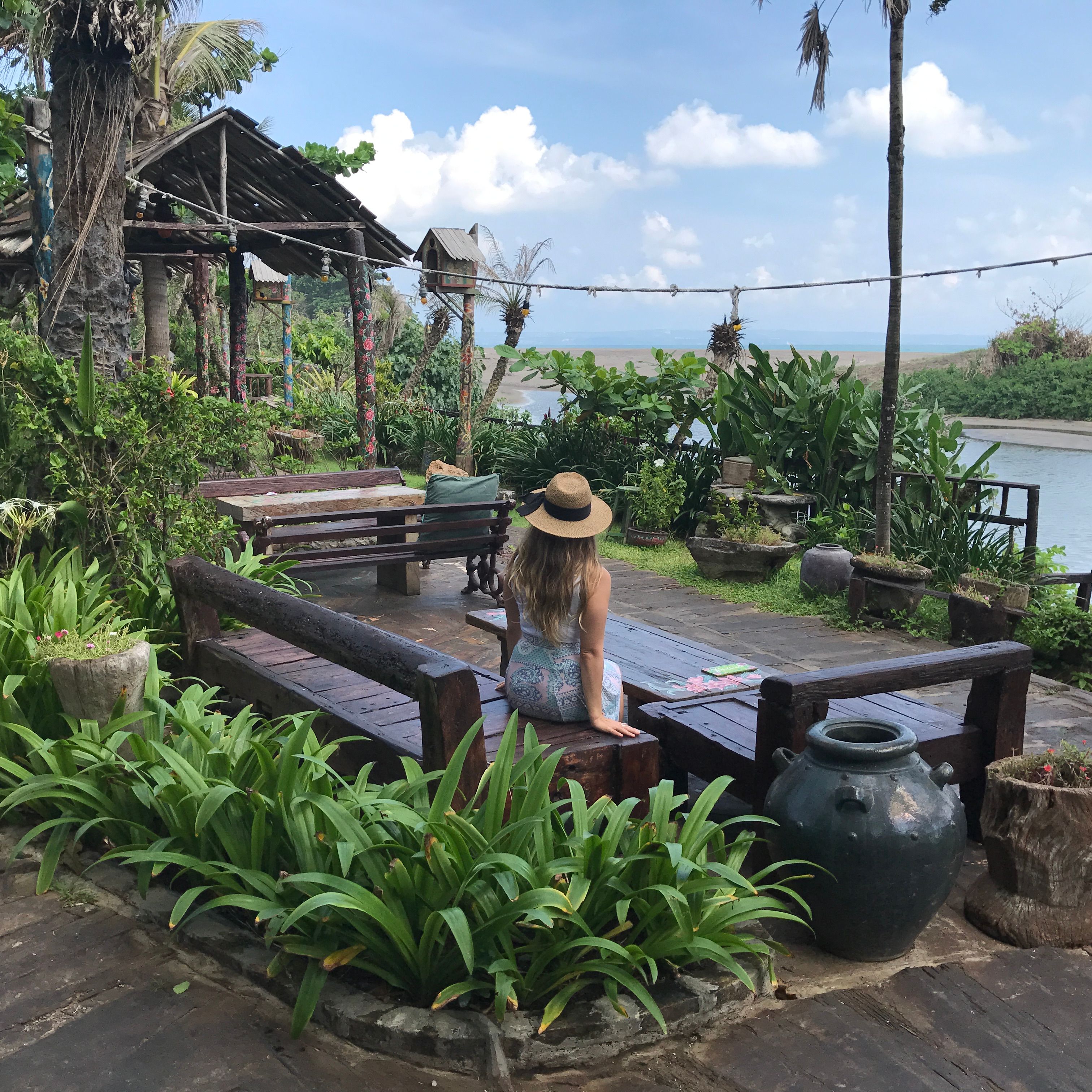 A photo of Rebecca Michelle a personal mindfulness coach from nyc. She is facing away looking at the water in Bali and has a beige hat on.