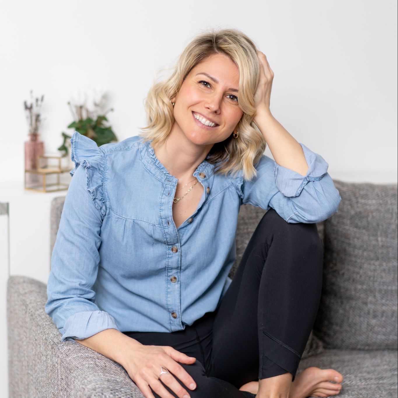 A photo of Rebecca Michelle an online mindfulness coach is sitting on a grey couch smiling.
