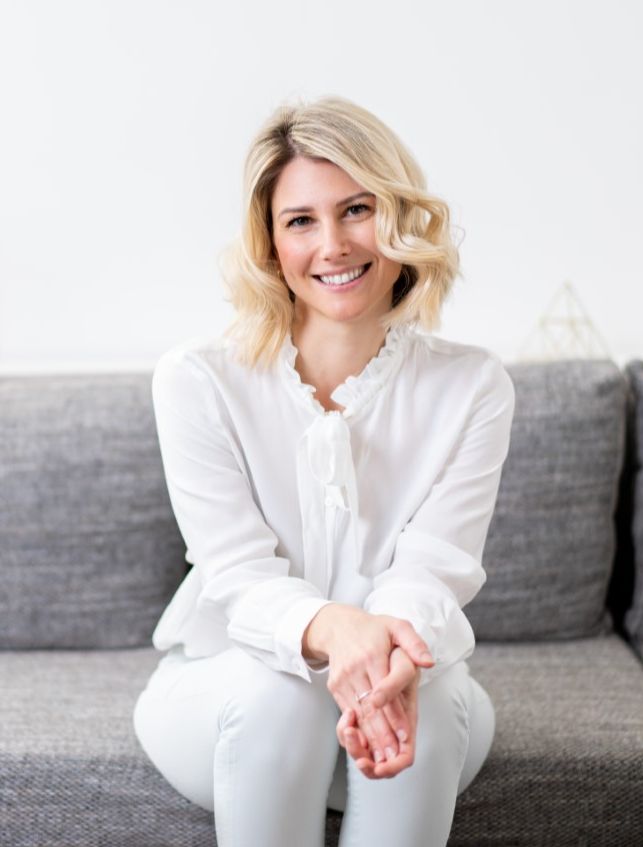 A photo of Rebecca Michelle, meditation teacher sitting on a coach smiling.