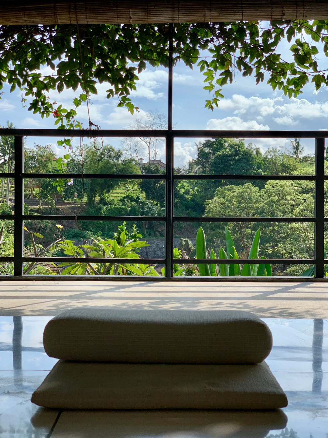 A photo of where Rebecca Michelle, mindfulness coach would sit for meditation in her bali meditation program. There is a meditation cushion and a blue sky and green jungle plants in the background.