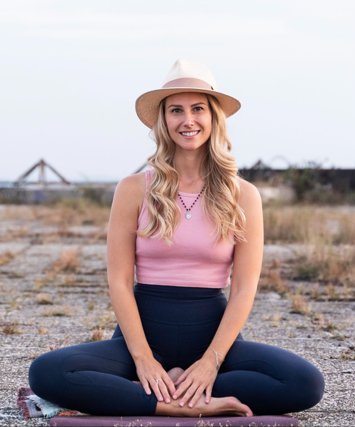 Photo of Rebecca Michelle, meditation coach who offers meditation classes online is sitting outside in cross legged meditation seat and smiling.
