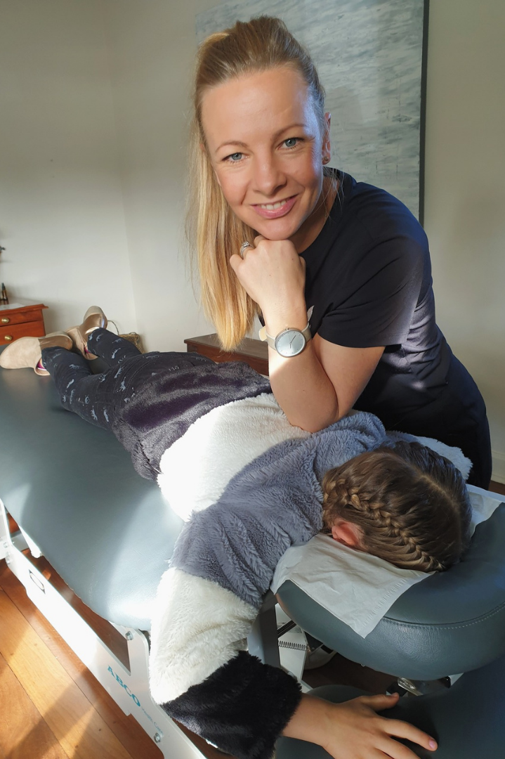 Nicola Wearne demonstrating a soft tissue technique with a person lying face down on a treatment table.