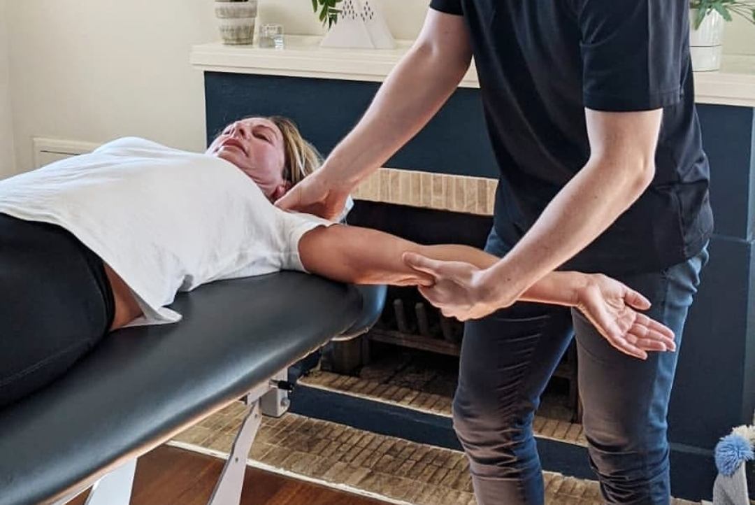Practitioner supporting an outstretched arm during shoulder and upper-limb soft tissue work.