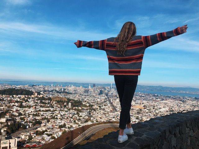 A teenager with arms outstretched overlooking the San Francisco skyline