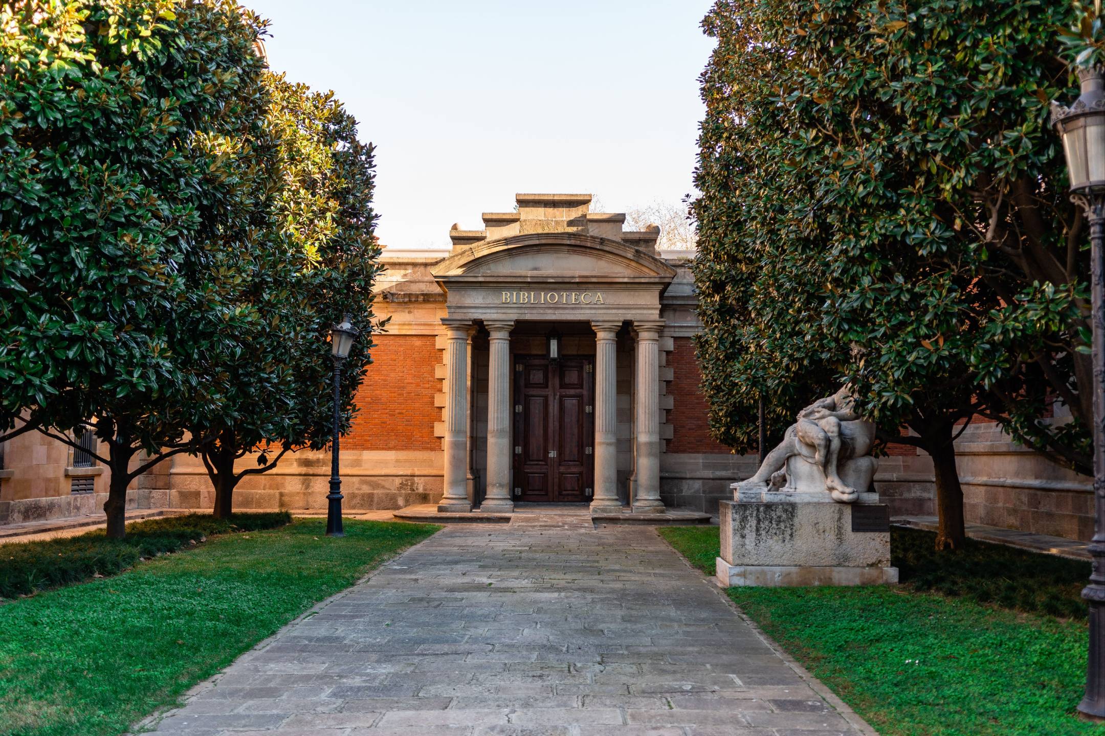 A stone library entrance with columns and a pediment, seen along a path between magnolia trees