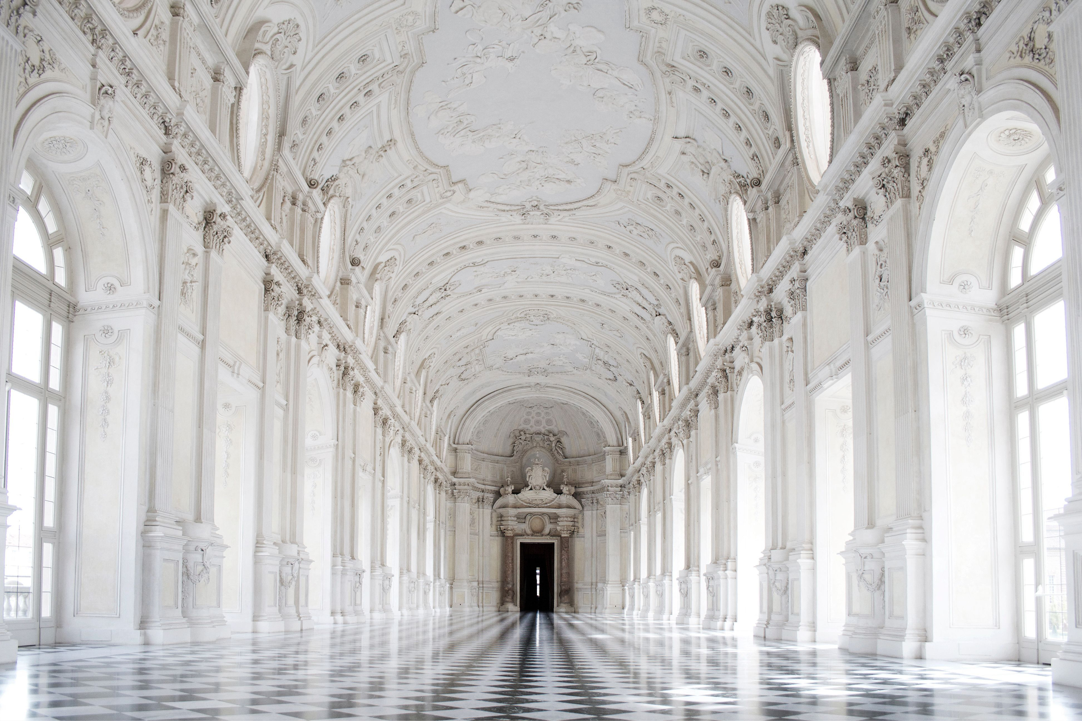 A long marble gallery in white stucco, its checkered floor receding toward a single open door