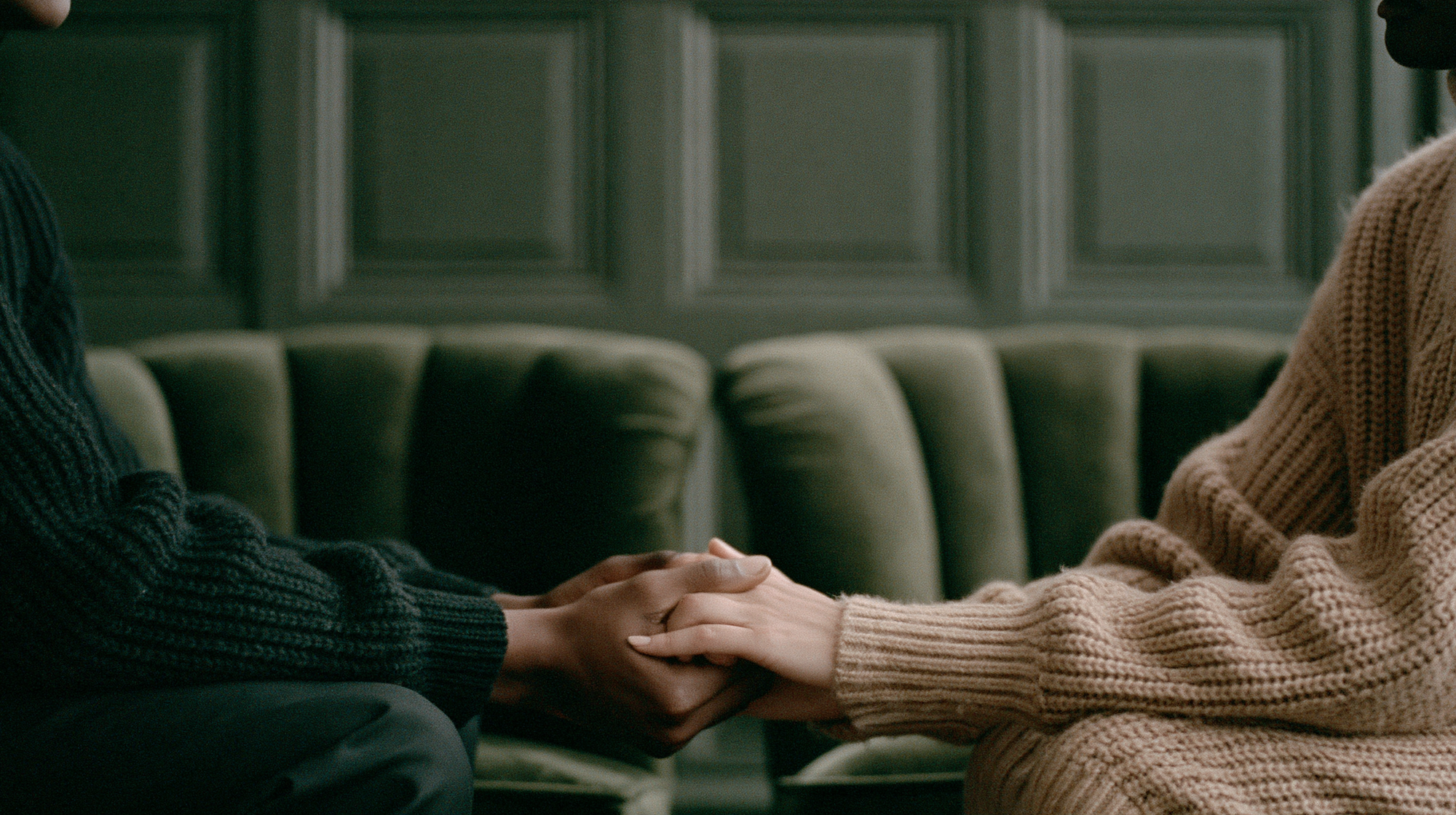 Two people holding hands on a sofa in a sunlit room