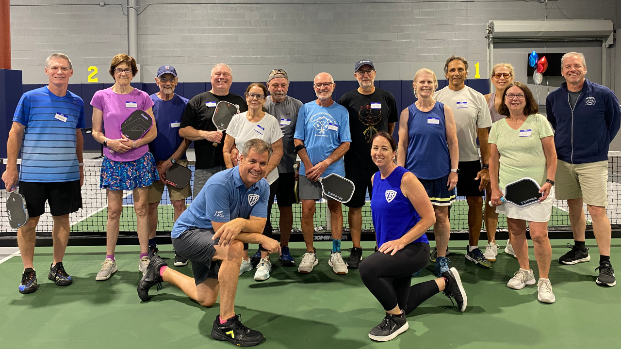 Tony Roig and Kyleen Dye with a group of campers posed on an indoo court at a TRP pickleball camp