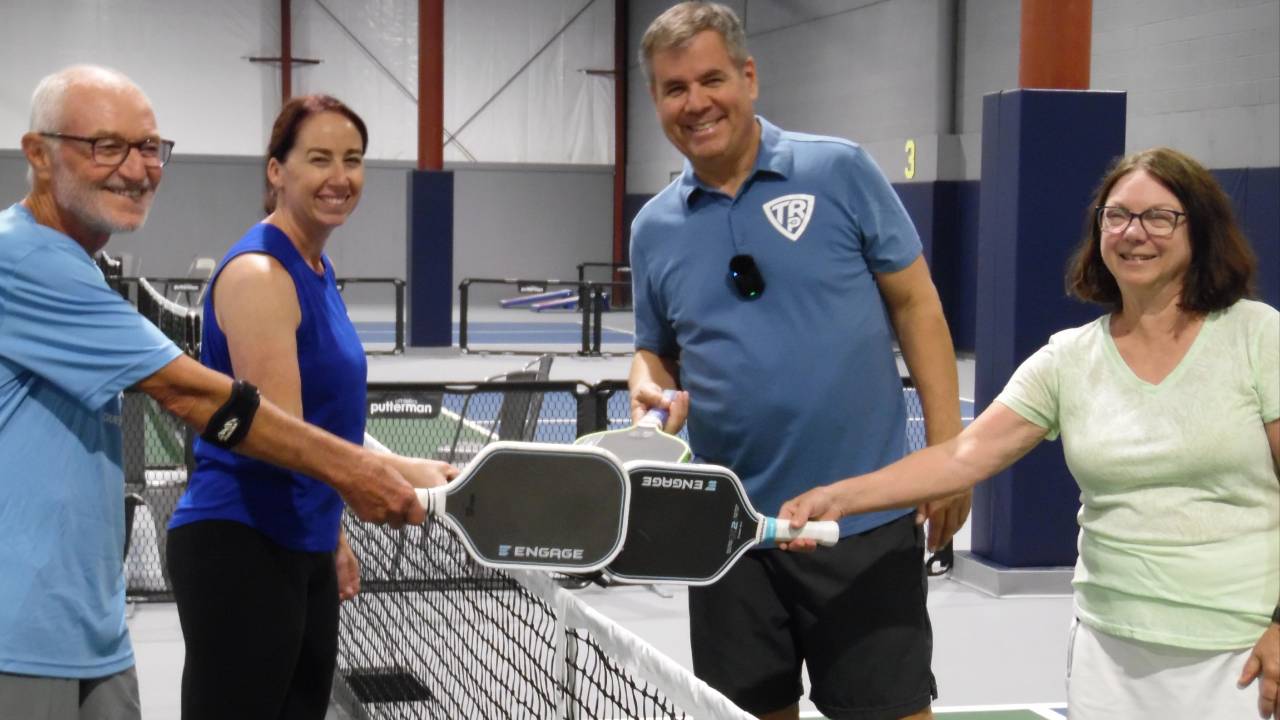 Four pickleball players tapping paddles at the net after a game on an indoor court