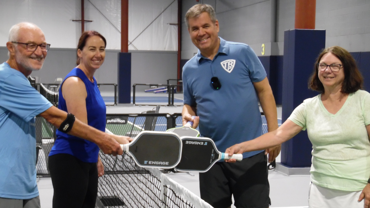 Tony Roig and Kyleen Dye with pickleball players tapping paddles at an indoor pickleball camp