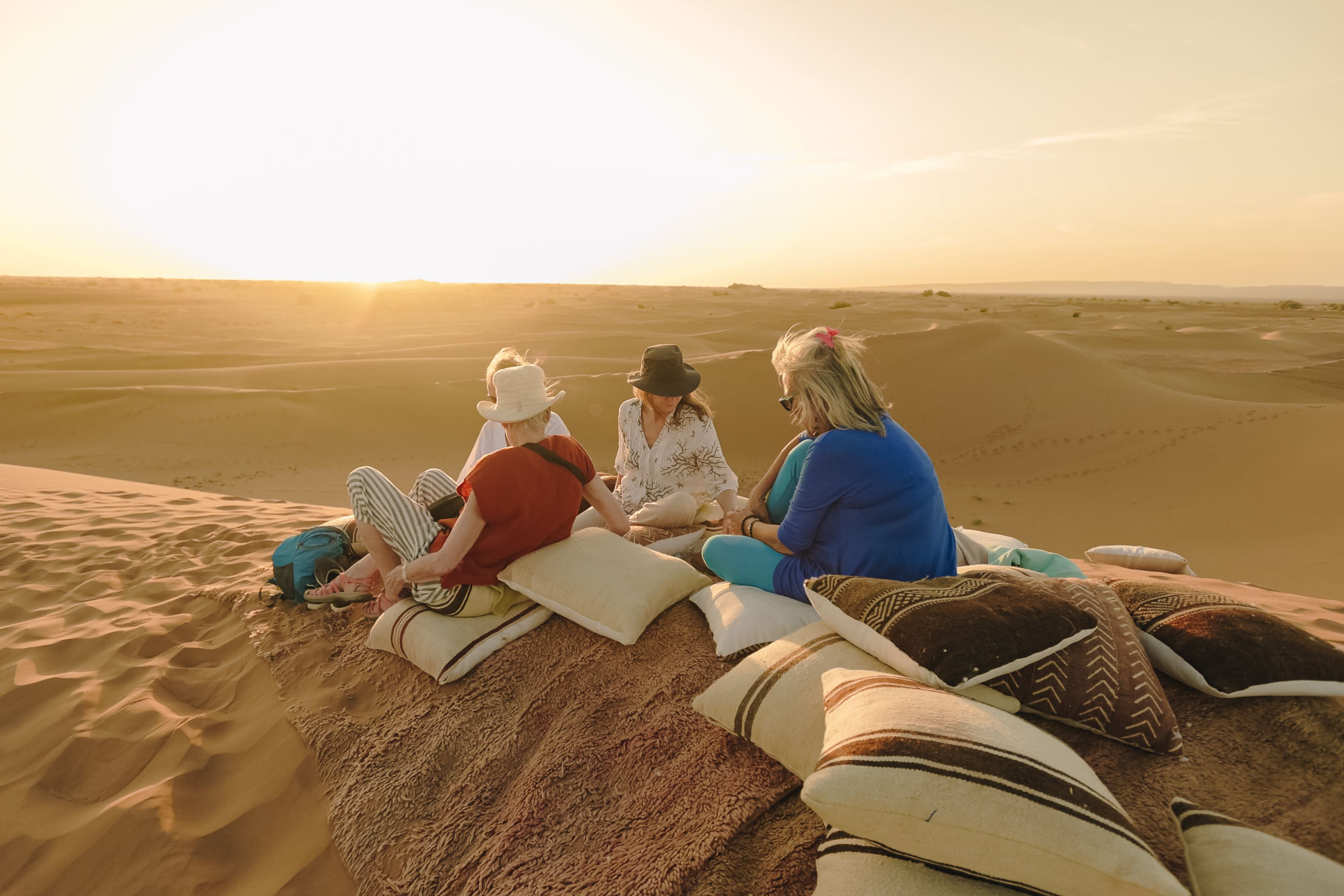 A group of women sitting on scattered cushions atop a sand dune in the Sahara desert